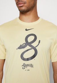 Camiseta amarilla de manga corta de Nike con un diseño de serpiente negra y la palabra "Serpientes" en cursiva debajo. Tela suave, corte clásico.