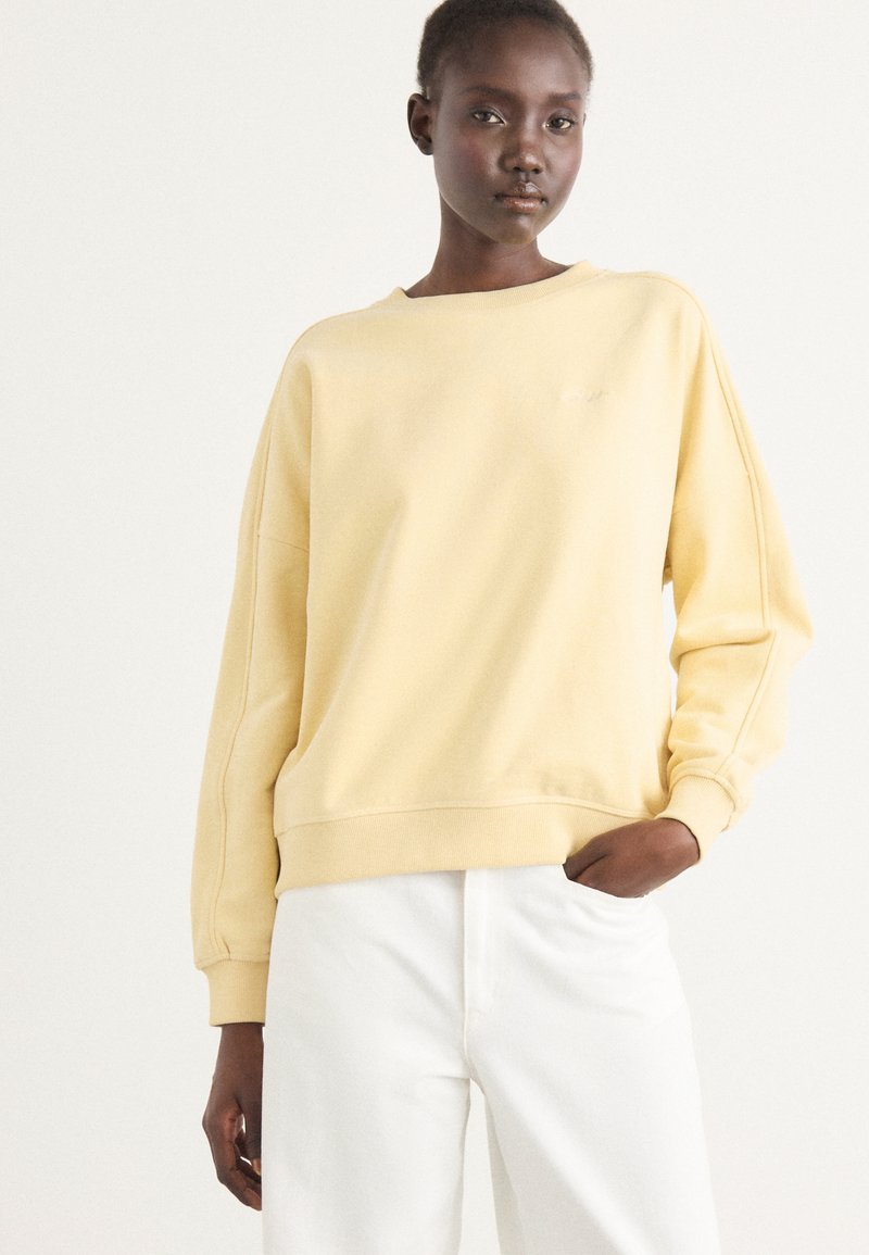 Gul oversized sweatshirt med rund halsringning, ribbad mudd och nederkant. Matchas med vita högmidjade byxor. Slät bomullsduk.
