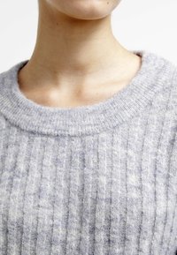 Světle šedý pletený svetr s ribkovanou texturou, širokým kulatým výstřihem a jemnými variacemi odstínu. Měkký materiál s mírně chmýřitou úpravou.