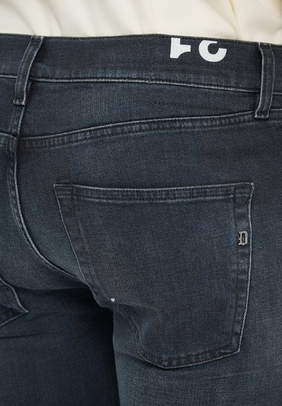 Mörk denimjeans har en femfickorsdesign med synlig sömnad. Midjebandet har en logotyp och tyget visar små texturvariationer.