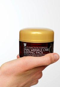 Barattolo di maschera da notte per la cura delle rughe con chiusura dorata e corpo rosso scuro, con testo bianco sull'etichetta, tenuto in una mano.