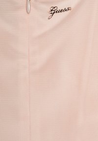 Ροζ διαφανές ύφασμα με διακριτή υφή, διαθέτει κεντρική ραφή και μεταλλικό λογότυπο "Guess" ραμμένο κοντά στην κορυφή.