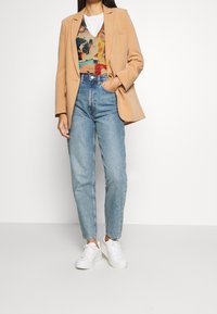 Béžové na míru ušité sako přes barevný svetr s vzorem, doplněné světle modrými džínami s vysokým pasem a bílými teniskami.