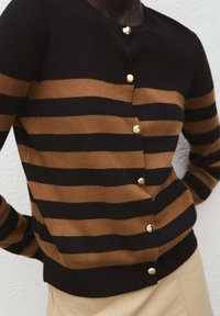 Gestreifter Cardigan in Braun und Schwarz aus Strickstoff, mit goldenen Knöpfen vorne und festen gerippten Säumen und Bündchen.