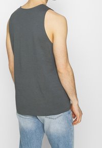 Grå ärmlös tanktopp i en mjuk bomullsblandning, med avslappnad passform och rena kanter. Bärs med ljusblå denimjeans.