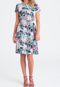 Kukkamekko, jossa on lyhyet hihat, istuva vyötärö ja levenevä helma. Kangas on värikkäällä trooppisten lehtien kuvioinnilla vaalealla pohjalla.