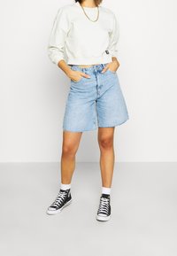 Sudadera blanca corta, pantalones cortos de mezclilla azul claro con dobladillo deshilachado y zapatillas altas negras con suelas y cordones blancos. Diseño minimalista.