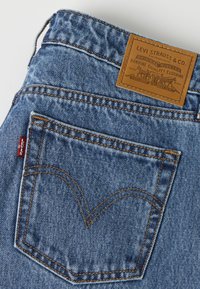 Poche arrière d’un jean en denim bleu avec couture orange, étiquette rouge Levi's et étiquette en cuir marron Levi Strauss & Co. sur la ceinture.