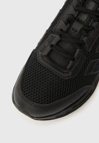 Sort atletiksko med mesh-overdel med læderdetaljer, snørelukning og en tekstureret gummisål.