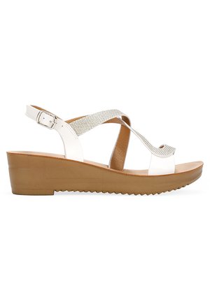 Sandales à talon compensé avec une tige en cuir blanc et un design entrecroisé. Caractéristiques d'une bride métallique et d'une semelle texturée marron pour l'adhérence. Fermeture à boucle.