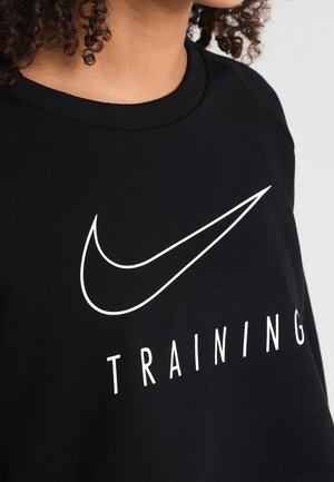 Nahaufnahme einer Person, die ein schwarzes Shirt mit weißem Nike-Swoosh-Logo trägt, unter dem das Wort "TRAINING" gedruckt ist.