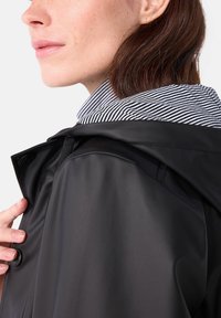Zwarte waterdichte jas met een hoge kraag, voorzien van een gestreepte binnenvoering, een gladde textuur en verstelbare trekkoorden.