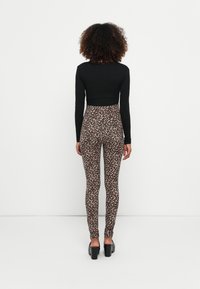 Haut noir à manches longues assorti à des leggings léopard taille haute, avec une texture lisse et une coupe près du corps. Chaussures à talons noires.