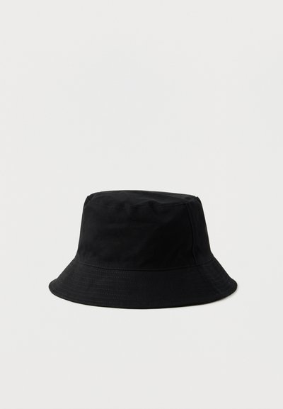 Μαύρο βαμβακερό καπέλο τύπου μπούκετ με ραμμένη φαρδιά γείσο και επίπεδη κορυφή σε απλό φωτεινό φόντο.