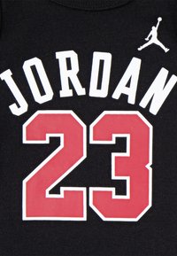 Must musta spordisärk, millel on valge "JORDAN" tekst ja selle all punase numbriga "23", mille ümber on valge ääristus, ning väikese Jordani logoga.