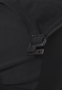 Tissu noir avec une texture lisse et extensible, doté d'un petit fermoir en plastique noir et de coutures nettes le long du bord.
