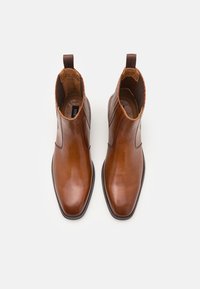 Botines de cuero marrón con punta afilada, paneles laterales elásticos y una lengüeta para ponérselos fácilmente. Acabado suave con sutiles acentos de textura.
