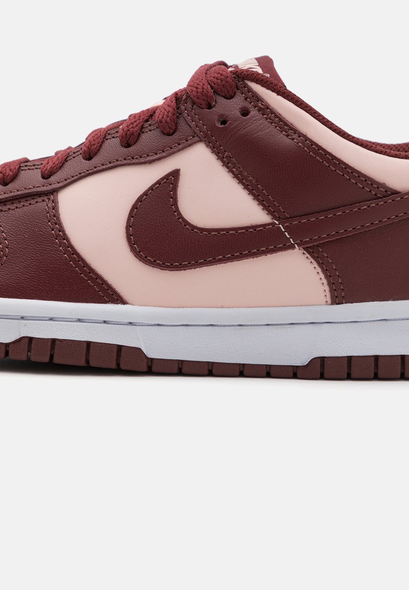 Nike-Sneaker mit oberem Teil aus kastanienbraunem Leder, hellrosa Akzenten, strukturierten Oberflächen und einer weißen Gummisohle mit einem gemusterten Profil.