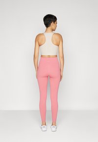 Reggiseno sportivo beige aderente e leggings rosa a vita alta, entrambi a costine, indossati con sneakers bianche. Inquadratura sulla vista posteriore e con elementi di design minimi.