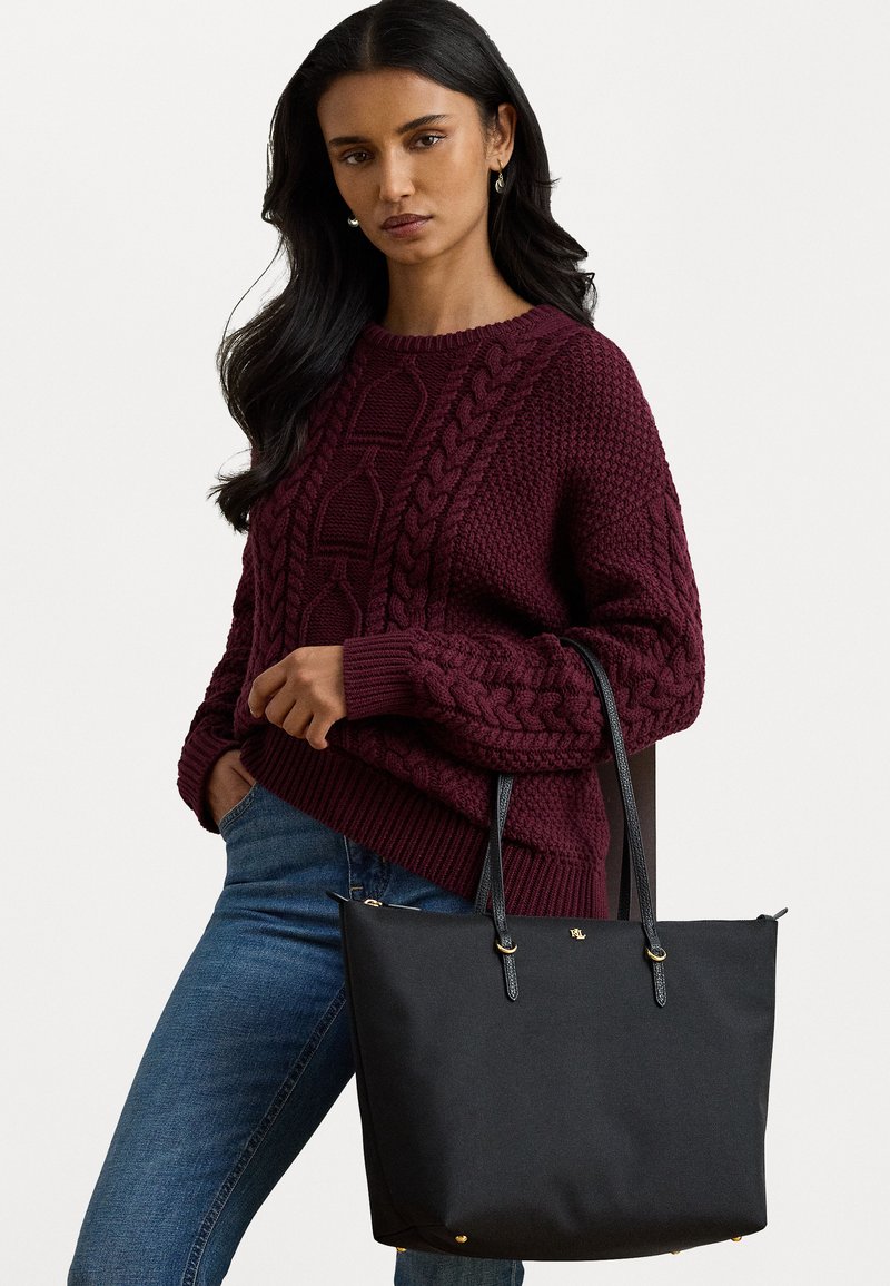 Juodas grandininės formos maišelis, pagamintas iš lygios medžiagos, su dviem ilgais odiniais diržais, auksinėmis detalėmis ir logotipu priekyje.