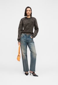 Γκρι, υφασμάτινος φούτερ με υφή και ριμπ μανσέτες, σε συνδυασμό με ξεθωριασμένο μπλε τζιν παντελόνι με φαρδιά πόδια. Το μοντέλο κρατά μια πορτοκαλί τσάντα χειρός και φορά μαύρα παπούτσια με τακούνι.