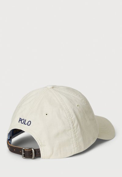 Bežinės medvilnės beisbolo kepuraitė su mėlyna siuvinėta "POLO". Reguliuojama ruda odinė juosta su metaliniu užtrauktuku gale.