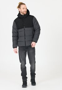 Polstret jakke i sort og grå med lynlås foran, hætte og kontrasterende paneler. Båret med mørke jeans og sorte støvler. Glat tekstur, afslappet design.