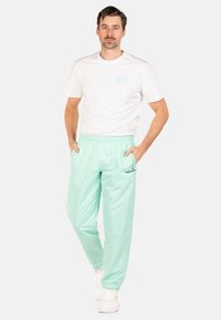 Mintgroene broek met elastische taille en zijzakken, taps toelopende boorden en een logo-accent; gecombineerd met een eenvoudige witte t-shirt met korte mouwen.