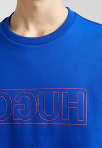 Felpa in cotone blu con colletto rotondo e polsini a coste, caratterizzata da un audace logo rosso "HUGO" racchiuso in un rettangolo sulla parte anteriore.