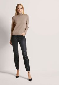 Beiger Rollkragenpullover kombiniert mit schwarzen Lederhosen und schwarzen spitzen Absatzschuhen, die eine figurbetonte Silhouette und glatte Textur zeigen.