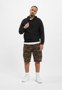 Mustat hupparit, jossa on kengurupussi, yhdistettynä camo cargo-shortsit. Valkoiset sukat ja lenkkarit täydentävät asua. Yksinkertainen, rento muotoilu.