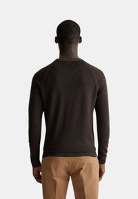 Maglione marrone a maglia con collo rotondo, maniche lunghe e polsini a coste. La texture è liscia, con un design aderente in vita e sulle spalle.