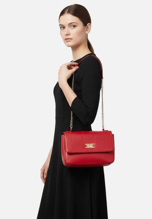 Borsa a mano in pelle rossa con una forma strutturata, dotata di una chiusura dorata, una tracolla a catena rimovibile e cuciture orizzontali sulla patta.