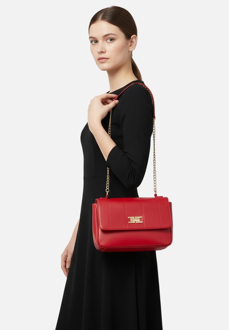 Borsa a mano in pelle rossa con una forma strutturata, dotata di una chiusura dorata, una tracolla a catena rimovibile e cuciture orizzontali sulla patta.