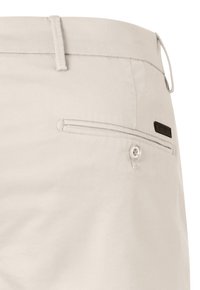 Beige Hosen mit einer glatten, strukturierten Oberfläche. Verfügt über eine Gesäßtasche mit einem Knopfverschluss und einem kleinen Markenschild in der Nähe der Tasche.