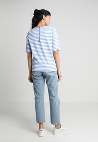 Lyseblå stribet kortærmet T-shirt med knapdetalje bagpå, parret med lysvaskede slidte jeans og hvide sneakers.