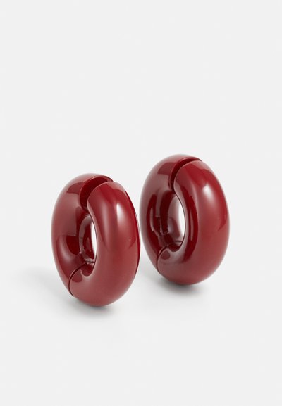 Pendientes de resina roja y brillante en un diseño circular con un detalle recortado. Textura suave y forma moderna, adecuados para un uso casual o formal.