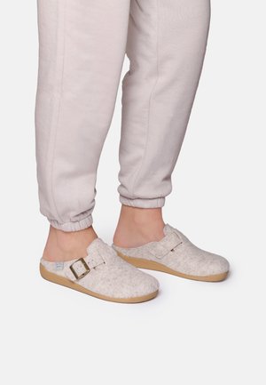 Sabots en feutre gris clair avec un bout rond et un accent en boucle, montés sur une semelle en caoutchouc beige ; associés à un pantalon jogging gris clair avec des poignets élastiques.