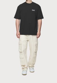 Czarny bawełniany t-shirt z małym logo na piersiach, w połączeniu z beżowymi spodniami cargo z wieloma kieszeniami i luźnym krojem.