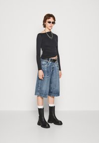 Top negru cu maneci lungi, cu textură plisată, culotte din denim albastru oversized, cizme negre cu toc gros, și ochelari de soare mici. Colier din lanț argintiu.