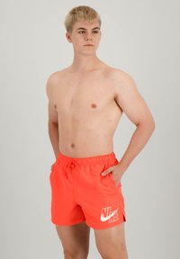 Piros Nike úszónadrág, rugalmas derékkal és zsinórral, fehér logóval a bal lábon és oldalsó zsebekkel.