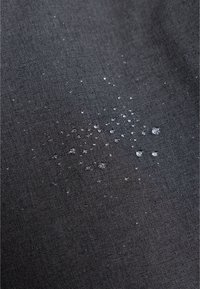 Zwarte stof met een gestructureerd oppervlak, met waterdruppels verspreid eroverheen. De druppels creëren een contrast tegen het materiaal.