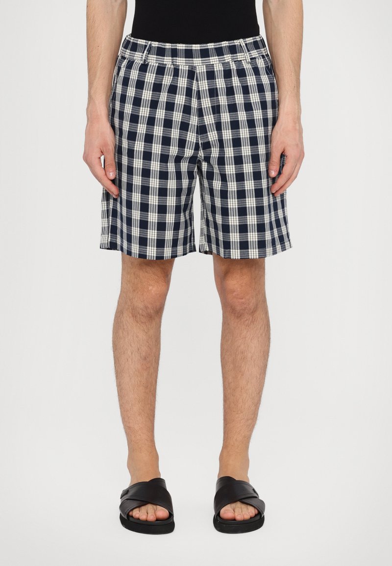 Navy og hvit rutete shorts, til knærne, elastisk midjebånd, bomullsblandingsstoff, parret med svarte sandaler.