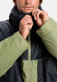 Padded jacket featuring a black and green color scheme. High collar with adjustable closure, textured fabric, and secured cuffs.