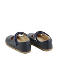 Zapatos Mary Jane de cuero azul oscuro con punta redondeada, tira de velcro y suela flexible de color marrón claro. Incluyen detalles de costura decorativa.