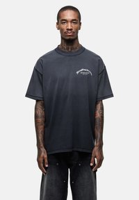 Czarnoszary oversize t-shirt z krótkim rękawem, z białym logo na lewej piersi, wykonany z miękkiego, strukturalnego materiału.