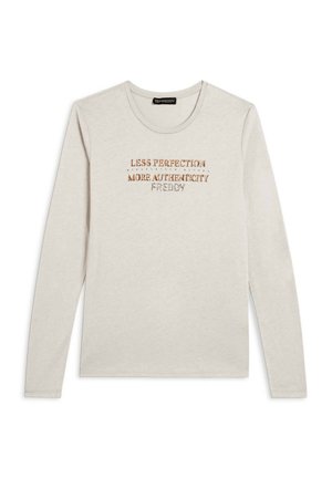 Camicia a maniche lunghe in cotone beige chiaro con collo rotondo. Presenta testo stampato in oro metallico e marrone: "MENO PERFEZIONE PIÙ AUTENTICITÀ."