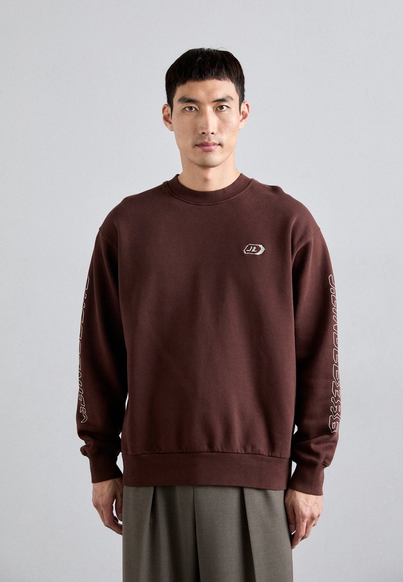 Καφέ φούτερ από βαμβακερό μείγμα, με μακριά μανίκια, στρογγυλή λαιμόκοψη και λογότυπο στο στήθος με κείμενο κατά μήκος του μανικιού.