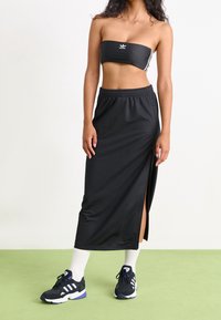 Černý bandeau top s bílými akcenty, spojený s dlouhou černou sukní s vysokým rozparkem, nošený s černými sportovními botami a bílými pono žkami.