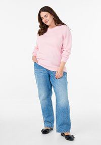 Pullover sweatshirt rosa chiaro con texture e scollatura rotonda, abbinato a jeans blu a vestibilità ampia e scarpe flat nere con dettaglio a fiocco.